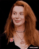 a woman with red hair wearing a necklace and hoop earrings .