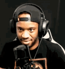 a man wearing headphones and a hat is standing in front of a microphone and smiling .