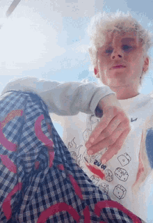 a young man wearing a white shirt with dice on it and plaid pants