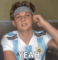 a young man wearing a headband and a soccer jersey says yeah