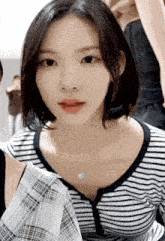 a woman wearing a striped shirt and a blue necklace looks at the camera