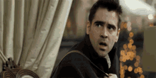 a man in a black jacket is standing in front of a curtain and looking at something .