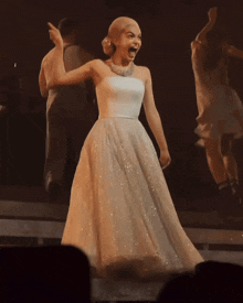 a woman in a white dress is standing on a stage with her arms in the air