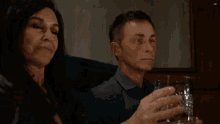 a man and a woman are toasting with glasses of whiskey in front of an ad
