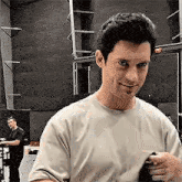 a man in a white t-shirt is standing in a room with a man in a black shirt behind him .