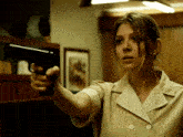 a woman in a tan jacket is pointing a gun