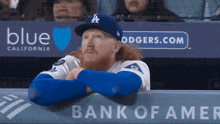 a baseball player sitting in the dugout with a blue california ad behind him