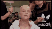 a woman with a bald head is getting her makeup done by someone wearing an adidas apron