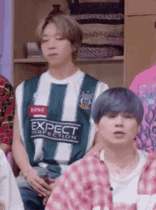 a group of people are sitting in a room and one of them is wearing a shirt that says expect perfection