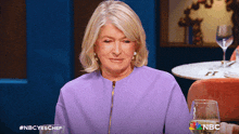 a woman in a purple jacket is sitting at a table with a glass of wine in front of her