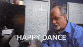 a man in a blue shirt is sitting at a desk with the words " happy dance " above him