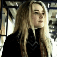 a woman with long blonde hair wearing a black turtleneck and a scarf