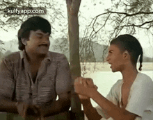 a man and a boy are sitting under a tree holding hands and talking to each other .