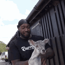 a man wearing a raw boy shirt holds a small sheep