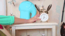 a woman is playing with an alarm clock on a night stand