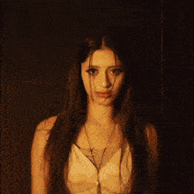 a woman with long hair and a necklace is standing in a dark room