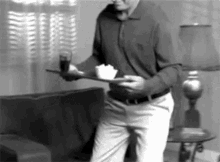 a man is standing in a living room holding a tray of food and a glass of soda .