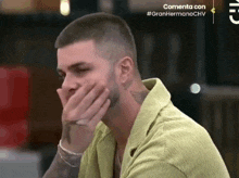 a man in a green shirt covering his mouth with his hands