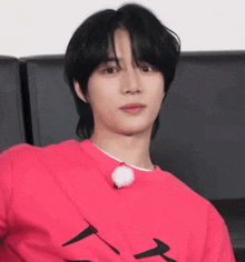 a young man with long black hair is wearing a pink shirt with the letter a on it