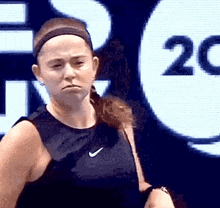 a woman wearing a headband and a black tank top is standing in front of a large screen with the number 20 on it .