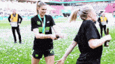 two female soccer players are standing on a field with a bottle of beer in their hand
