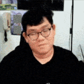 a man wearing glasses and a black shirt is sitting in front of a microphone