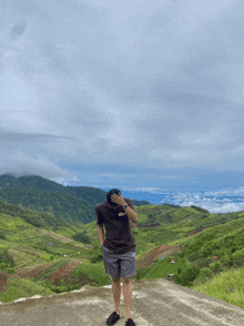 a man covering his face while standing on a hill