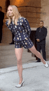 a woman in a blue jacket and shorts is standing with one leg up