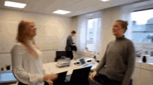 two women are standing in a room with a laptop on a desk