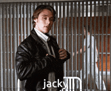 a man in a leather jacket and tie is standing in front of a fence with the word jacky written on it