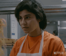 a woman wearing an apron and an orange shirt with netflix written on the sleeve