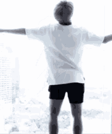 a man in a white shirt and black shorts is standing in front of a large window .