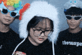 a girl wearing glasses and a hat is standing next to two boys wearing sunglasses and a rainbow wig .