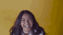 a woman is laughing with her hair blowing in the wind in front of a yellow wall .