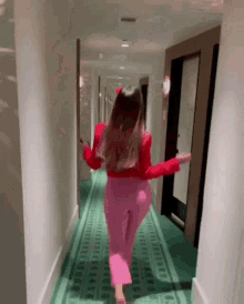 a woman in a red top and pink pants is walking down a hallway .