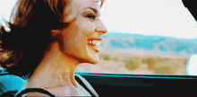 a woman is smiling while sitting in a car