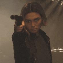 a woman in a black jacket is holding a gun