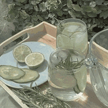 a wooden tray with glasses of water , lemons , cucumbers , and rosemary on it .