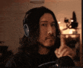 a man with long hair is wearing headphones and pointing up