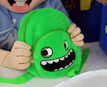 a person holding a green backpack with a cartoon face on it