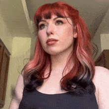 a woman with red hair and black streaks is wearing a black tank top .