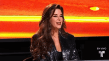 a woman in a sequined jacket is sitting in front of a large screen .