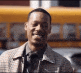 a man in a plaid jacket and tie is smiling in front of a yellow bus .