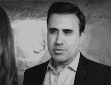 a black and white photo of a man in a suit talking to a woman .