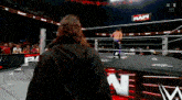 a man in a black cape is standing in a wrestling ring with a crowd watching .