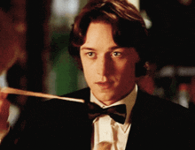 a young man in a tuxedo and bow tie looks at something