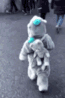 a person dressed as an astronaut is walking down the street holding a stuffed animal .