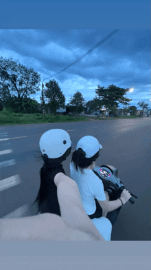 two women wearing white helmets are riding a motorcycle down a street