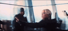 a woman is holding a gun in front of a window while a man stands behind her .