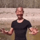 a bald man in a black shirt is standing in a body of water with his arms outstretched .